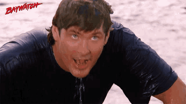 a man with water coming out of his mouth is wearing a black shirt with baywatch written on it