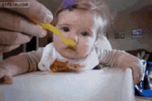 a baby is being fed with a yellow spoon by a person ..