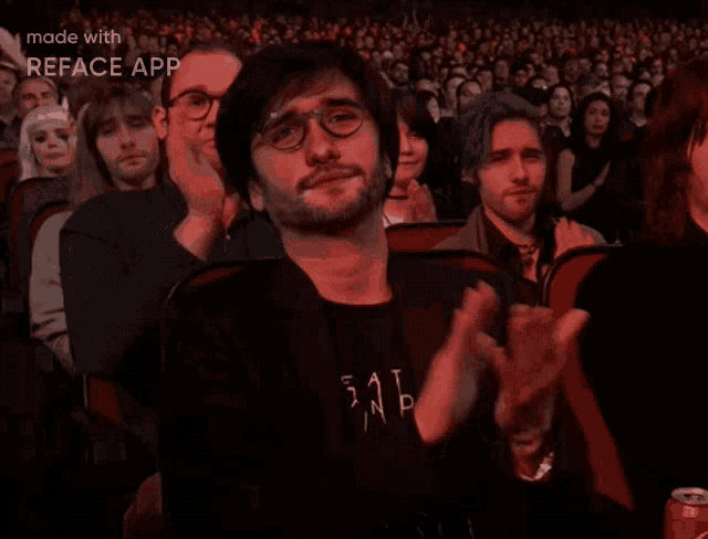 a man wearing glasses and a shirt that says 511 is clapping in a crowd
