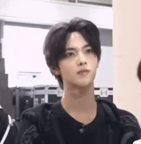 a young man with long black hair is wearing a black shirt and a black jacket .