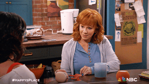 a woman sits at a table with a cup of coffee and a sign that says nbc
