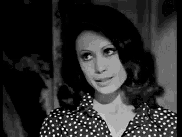a black and white photo of a woman wearing a polka dot shirt and hat .