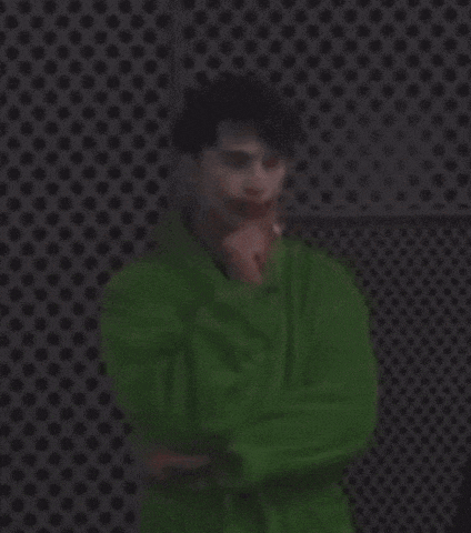 a man in a green robe is standing in front of a black wall with polka dots .