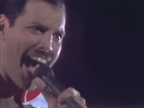 a close up of a man singing into a microphone with a mustache .