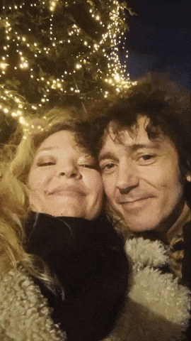 a man and a woman are posing for a picture in front of a tree with lights