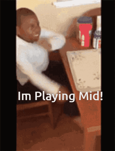 a man is sitting at a desk with the words im playing mid