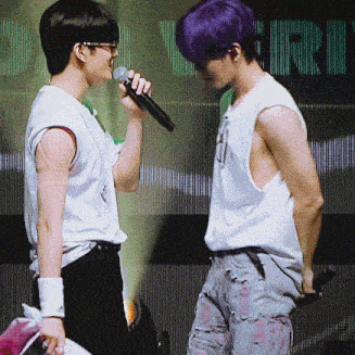 a man with purple hair is singing into a microphone while another man looks on