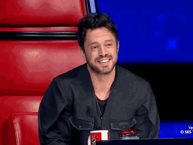 a man with a beard is smiling while sitting in front of a red chair