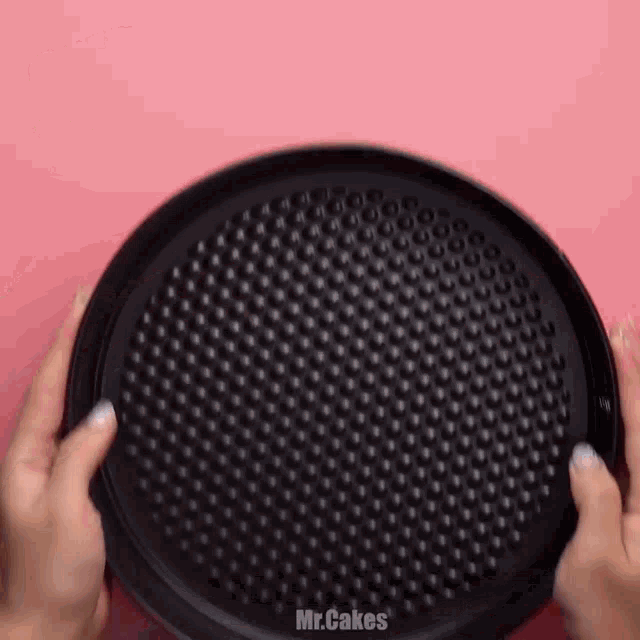 a person is holding a pizza pan in their hands on a pink surface .