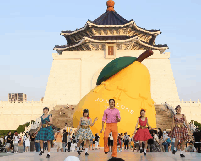 a group of people are dancing in front of a large pear shaped sculpture that says jo malone