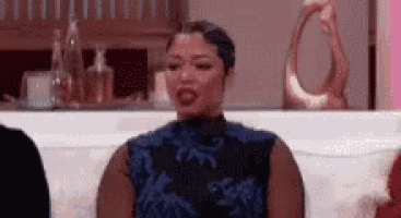 a woman in a blue dress is sitting on a couch and making a face .