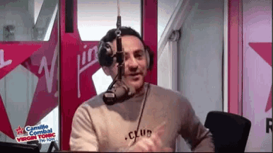 a man speaking into a microphone with camille combat virgin tonic on the wall behind him