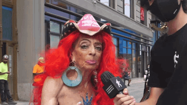 a woman with red hair is being interviewed by a man wearing a mask and a microphone with the letter k on it
