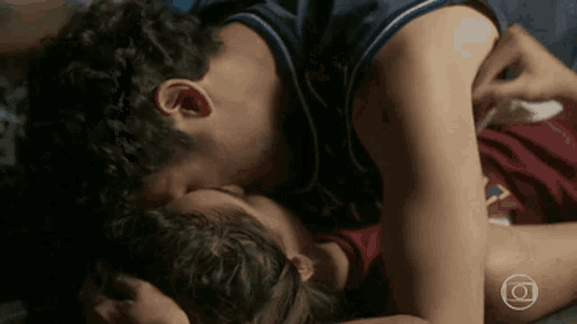 a man and a woman are kissing on a bed with the letters o on the bottom left