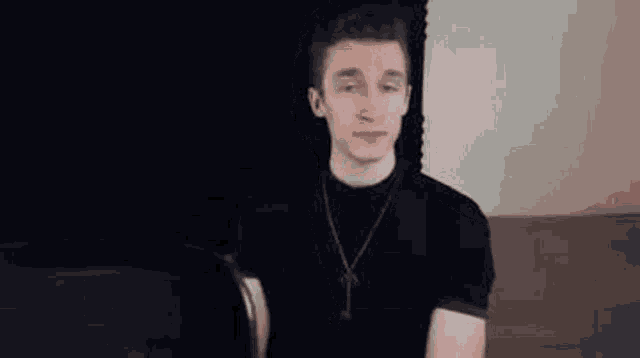 a young man wearing a black shirt and a necklace is sitting on a couch .