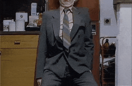 a man in a suit and tie is sitting in front of a refrigerator in a kitchen .