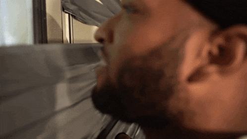 a man with a beard is looking out a window with his eyes closed