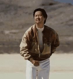 a man in a jacket and white pants is standing in a desert .