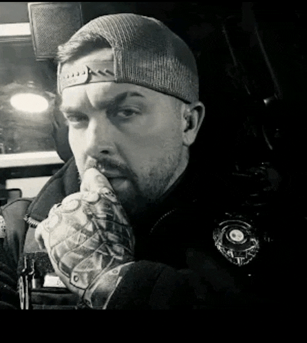 a man wearing a hat and gloves is sitting in a car with his hand on his mouth .