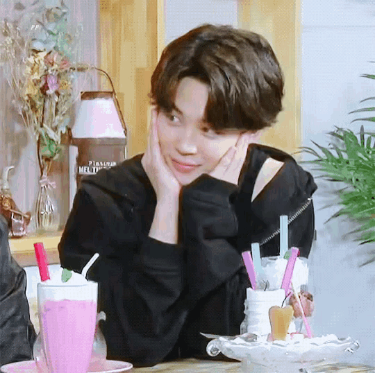 a young man is sitting at a table with a pink milkshake and straws