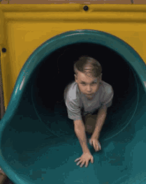 a young boy is crawling through a green tube on a slide