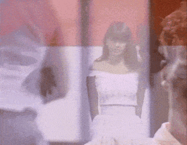 a woman in a white off the shoulder dress is standing in front of a red wall .