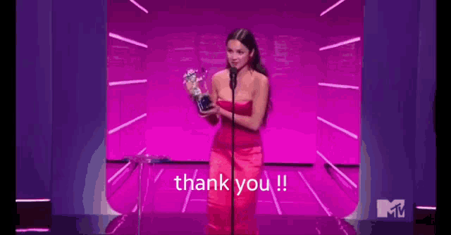 a woman in a red dress is kneeling on a stage with a microphone and holding a trophy and saying thank you