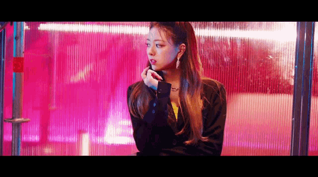 a woman is standing in front of a pink wall and applying lipstick .