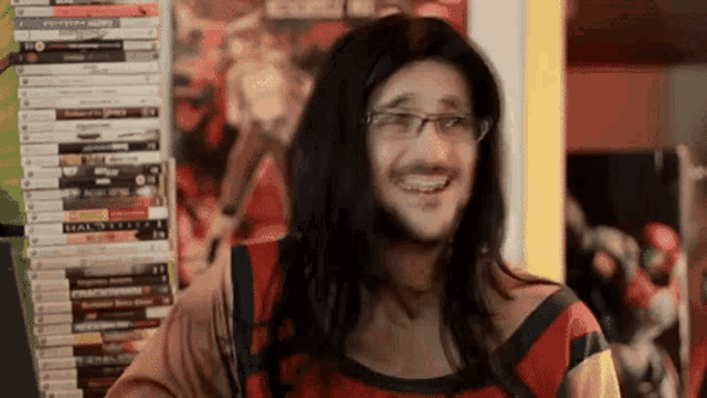 a man with long hair and glasses is smiling in front of a stack of video games