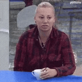 a woman in a red plaid shirt is sitting at a table holding a cup of coffee .