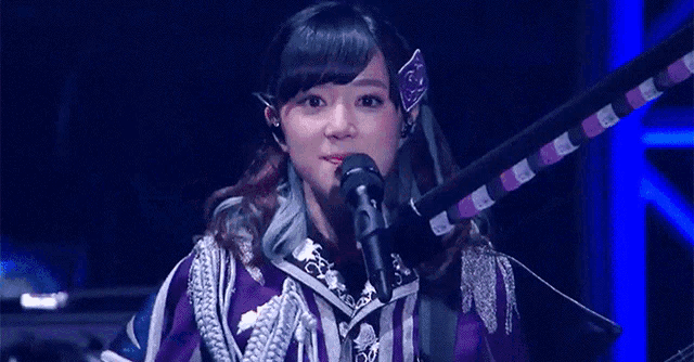 a woman in a purple jacket is singing into a microphone .