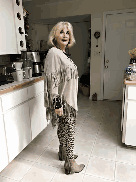 a woman standing in a kitchen wearing a fringed poncho and leopard print pants