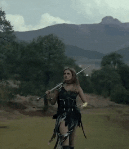 a woman is holding a sword in a field with mountains in the background