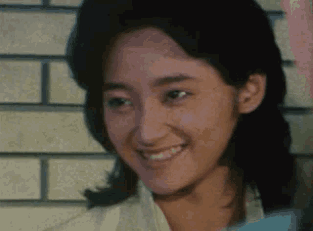 a woman is smiling in front of a brick wall and looking at the camera .