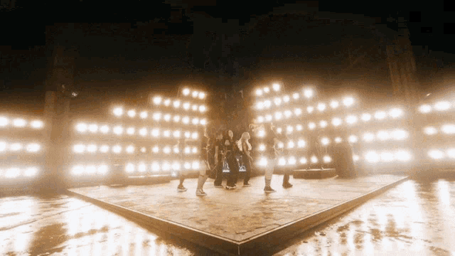 a group of people are dancing on a stage with a lot of lights