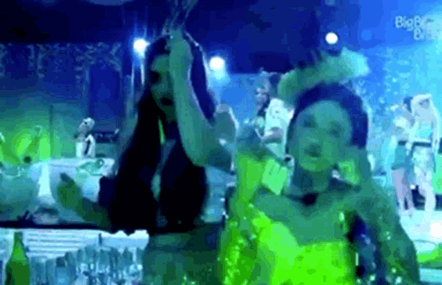 two women in green dresses are dancing in a dark room with a blue background .