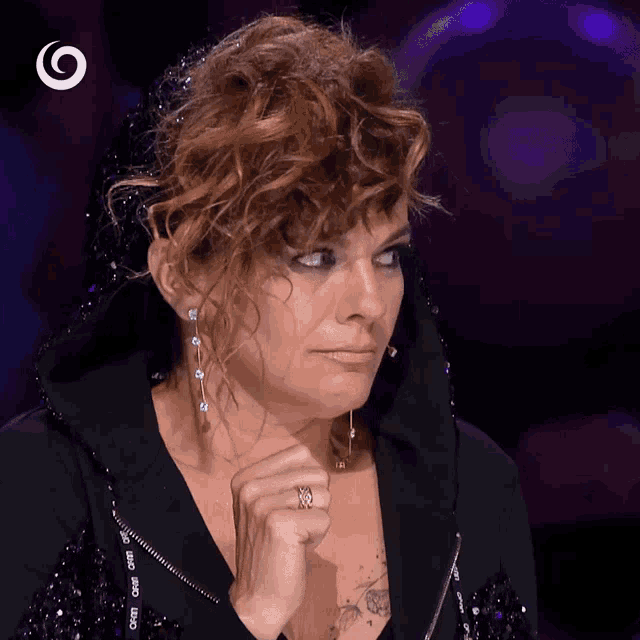 a woman with curly hair and a ring on her finger is wearing a black jacket with the word cmd on the front