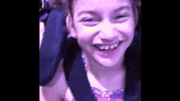 a little girl is smiling while sitting on a roller coaster .
