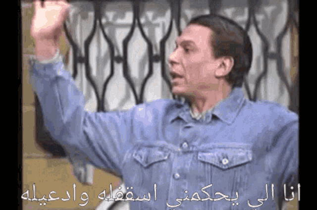a man in a denim jacket holds his hands up in the air