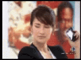 a woman is talking on a cell phone with a man in the background .