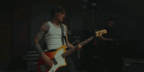 a man in a white tank top plays a guitar