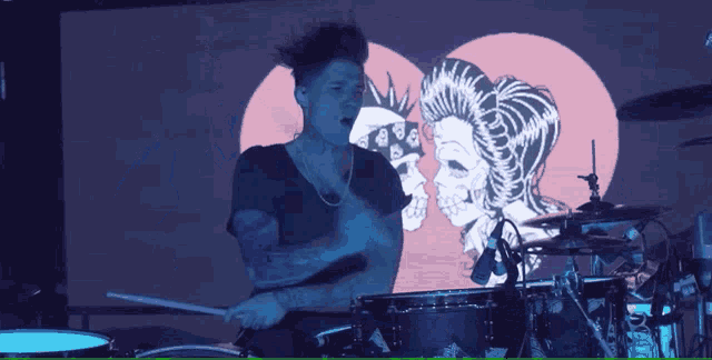 a man is playing drums in front of a screen with a skull and a woman on it