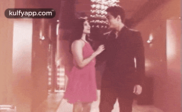 a man and a woman are standing next to each other in a hallway . the woman is wearing a pink dress .