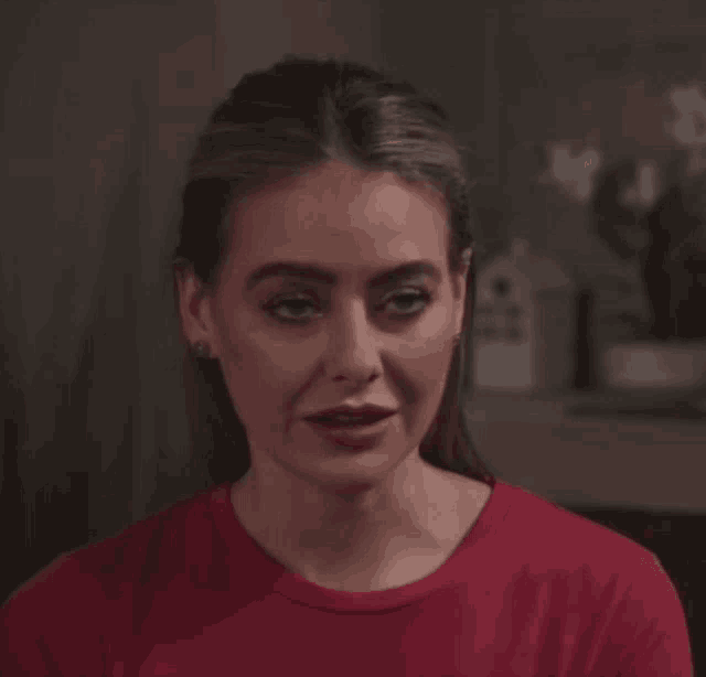 a woman in a red shirt looks at the camera with a serious look on her face