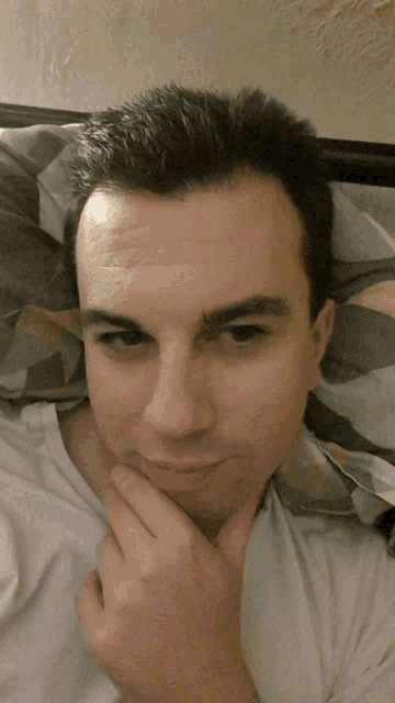 a man in a white shirt is laying on a bed with his hand on his chin
