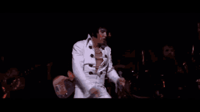 a man in a white suit is holding a guitar and singing into a microphone