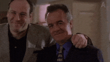 two men in suits and ties are posing for a picture and smiling for the camera .