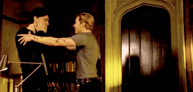 a man with a tattoo on his arm is hugging another man in a room