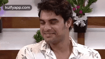 a man in a white shirt is smiling with his eyes closed in front of flowers .
