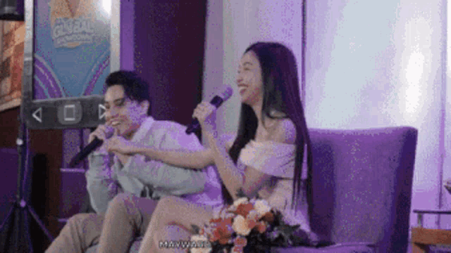 a man and a woman sitting on a couch with microphones